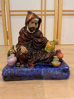 Front view of Royal Doulton The Potter figurine showing seated potter with various ceramic pieces on blue base.