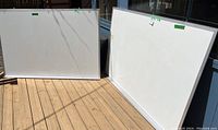 Photo of two large dry erase whiteboards placed on wooden floor outside in sunlight, showing size and condition.