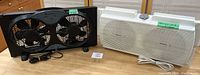 Photo of two window sill fans on a wooden table, black dual fan on the left and white single fan on the right.