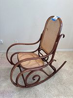 Side view of vintage bent wood rocking chair showing curved armrests, rocker base and woven rattan seat and backrest.