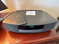 Front view of Bose Wave Music System powered on displaying time 11:20 on digital clock, with remote placed on top.