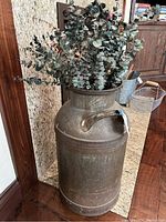 Brass milk container adorned with a bunch of dried eucalyptus leaves placed on its top, photographed from multiple angles highlighting texture and condition.