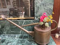 Full side view of brass watering can with flower arrangement on marble surface.