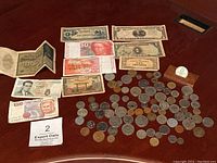 Overview image showing multiple foreign currency bills arranged above a large assortment of coins on a reddish surface.