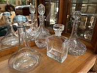 Four decanters on wooden surface in front of a mirror showing shapes and glass patterns.