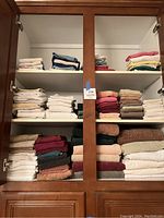 Photo of three shelves inside a wooden cabinet filled with folded towels in assorted colors including white, beige, burgundy, green, peach, and blue.
