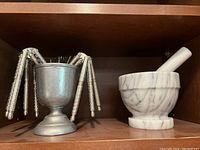 Nutcrackers arranged in a metal cup alongside a white marble mortar with pestle on a wood shelf