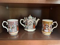 Front view of tea set with teapot and two beakers displayed on shelf