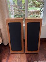 Front view of two floor-standing wood veneer speakers with black fabric grilles