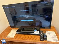 Front view of Sony TV on stand with DVD player below, remotes and manuals laid out