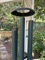 Close-up of the large green metal tubes and top ring of the wind chime hanging outdoors.