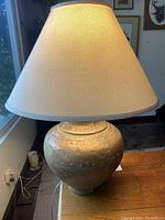 Full view of the vintage brass lamp with fabric lampshade on a wooden surface by a window.