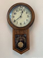 Front view of vintage Elgin wood wall clock showing clock face, wood case, and pendulum case.