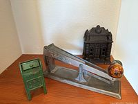 Full view of all three vintage metal items including mailbox, bank building, and egg scale.