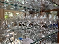 Image showing multiple rows of clear crystal wine glasses on glass shelves, including brandy snifters in foreground.