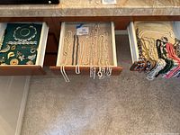 Three open drawers showing pearl and metal necklaces