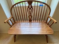 Front view of vintage oak wood bench showing curved spindle backrest with central carved splat and armrests.