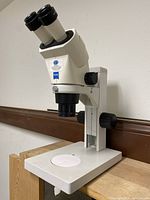 Side view of Zeiss stereo microscope on adjustable stand with white round stage plate and dual focus knobs