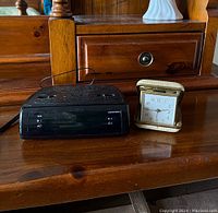Two alarm clocks on wooden surface, a vintage Europa travel alarm clock in folding beige/gold case and a black digital Neotech alarm clock.