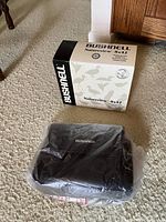 Photo showing the Bushnell Natureview 8x42 binoculars box next to the black carrying case wrapped in plastic.