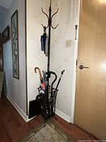 Full view of metal coat rack standing against a hallway wall with some umbrellas and a few items stored in the umbrella section.