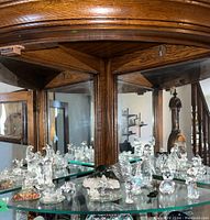 Wide view of crystal figurines on mirrored glass shelves inside a wooden and glass display cabinet.