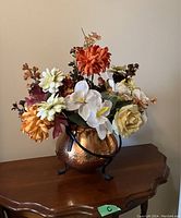 Front angled view of flower arrangement in brass pot on wooden table.