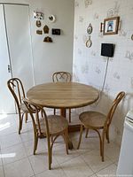 Full set of a round wooden kitchen table and four wooden chairs arranged in a kitchen corner.