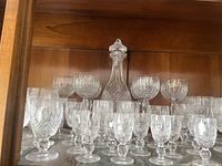 Wood-backed shelf with crystal decanter centered behind rows of stemmed glasses