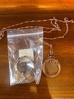 Photo showing two magnifying glass charm necklaces on a wooden surface, one loose in a plastic bag with chain, one assembled and decorated