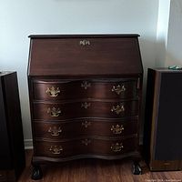 Front view of mahogany Jasper cabinet showing closed drop-front desk, four serpentine drawers with brass handles, claw feet.