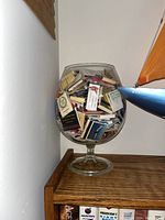 Front view of the large clear glass vase filled with numerous vintage match packs showing various colors and label designs.