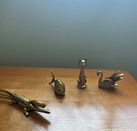 Photo of four brass animal figurines on wooden surface showing crocodile nutcracker, fish, cat, and swan.