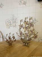 Photo of both ornate filigree caravel ship figurines on a wooden table showing relative size and details of sails and rigging.