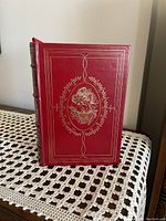 Front cover of the leather-bound book, showing red genuine leather with gold embossed floral design.