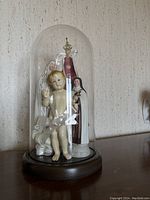 Front view of the religious figurines including infant Jesus and Virgin Mary inside the glass dome on a wooden base.