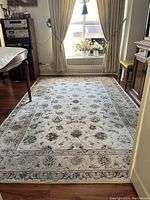 Rug laid out in a room with wooden flooring, showing full pattern and borders from a lower angle near a table and window.