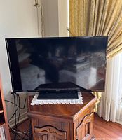 Full view of black Hitachi flat screen TV on a wood stand, screen off, showing size and condition.