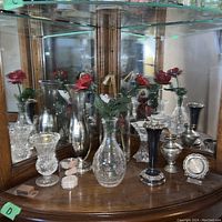 Photo showing the overall lot with multiple vases including clear crystal and silver-toned metal. Some vases have artificial red roses.