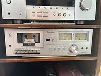 Photo of Technics RS-616 vintage stereo cassette deck with cassette loaded, analog VU meters, control buttons and knobs.