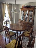 Wide view of oval wooden dining table with six yellow velvet-upholstered chairs around it, set on patterned rug under chandelier.