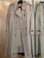 Full front view of beige London Fog trench coat hanging on a hanger showing double-breasted design and front details.