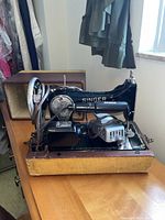 Vintage Singer sewing machine inside wooden casing with exposed operating parts including motor and needle plate, sitting on wooden surface.