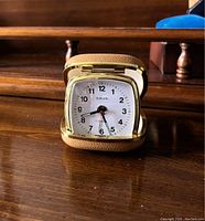 Open view of the vintage Europa travel alarm clock showing the white dial with black numerals and hands inside its beige textured folding case with gold trim.