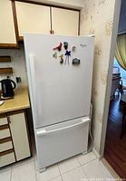 Closed view of the white Whirlpool refrigerator showing the top fridge door with various magnets and the bottom freezer drawer closed.