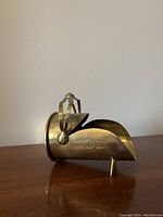 Side angle view of the brass shell casing trench art shaped as a helmet showing crest and engraved designs.