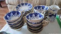 Stack of teacups and saucers showing blue leaf and vine floral pattern with gold trim on rims and handles.