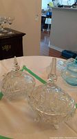 Two clear crystal candy pinwheel dishes with lids and footed feet on a table, showing overall size and presence.