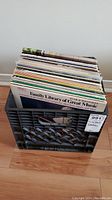 Black plastic crate filled with LP records in sleeves, viewed from above, with titles such as Family Library of Great Music visible.