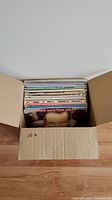 Top view of open cardboard box with multiple vinyl LP records inside, showing some album covers.